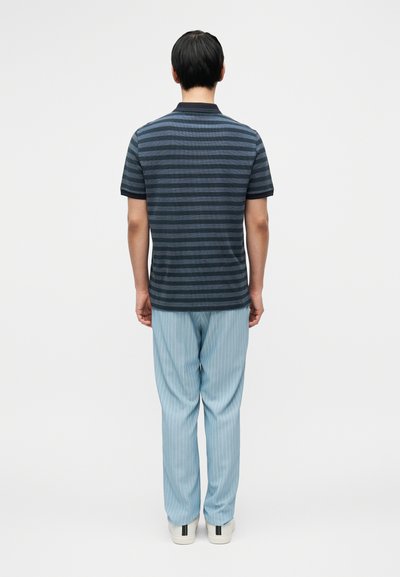Πολό μπλούζα με ναυτικό ριγέ σχέδιο και κοντά μανίκια, συνδυασμένη με ανοιχτόχρωμο γαλάζιο παντελόνι με λεπτές ρίγες και λευκά αθλητικά παπούτσια με μεταλλικές λεπτομέρειες.