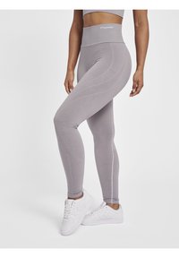 Høj talje grå leggings med teksturerede mønstre, tætsiddende pasform og elastisk materiale, parret med hvide træningssko.