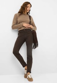 Brun sweater, mørkebrun slim-fit jeans og brune ruskinds sneakers med hvide snørebånd. En brun frynset taske hænger over hendes skulder.