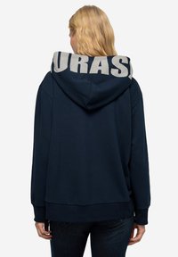 Marinblå hoodie med en stor grå logotyp "EURASIA" på huvan, med avslappnad passform, kenguruficka och ribbade ärmslut och nederkant.