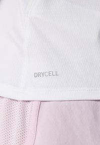 Biele športové tričko s mriežkovou textúrou a značkou DRYCELL, skombinované s lehkým ružovým materiálom pod ním, ktorý ukazuje hladké a priedušné materiály.