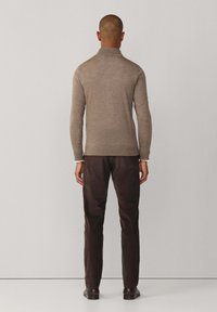 Grijze wollen pullover met een hoge kraag, een getailleerd ontwerp en lange mouwen, gecombineerd met donkerbruine broeken en zwarte schoenen. Eenvoudige, gestructureerde afwerking.