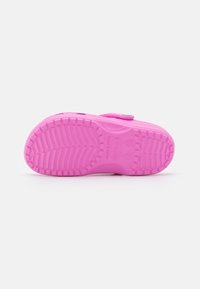 Pink Crocs sandals with a textured rubber sole, featuring a sturdy strap and a rounded design. Notable grip pattern on the sole.