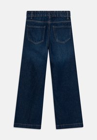 Jean bleu foncé à jambes larges avec taille élastique et deux poches arrière, vu de dos sur un fond uni.