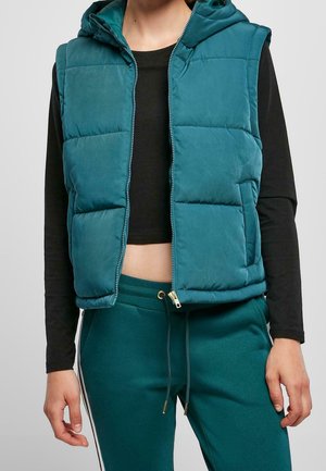 Teal gewatteerd vest met capuchon, voorzien van een rits en een doorgestikt patroon, met zijzakken. Gecombineerd met donkere groene joggers en een zwarte top.
