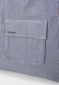 Niebieska i biała tkanina w paski z kwadratową kieszenią i logo "Barbour". Tekstura jest gładka, a na brzegach widoczne są szwy.