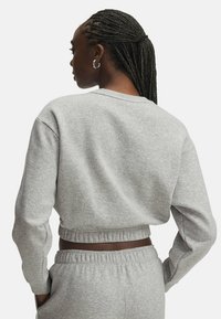 Sweatshirt gris court avec un col rond, une taille élastique et des manches longues. Fabriqué en matériau doux avec une texture lisse.