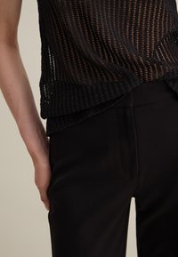 Black mesh top with a textured pattern, paired with fitted black pants. The top features a loose fit and side slit accents.