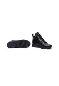Chaussures montantes en cuir noir avec œillets en métal et lacets, présentant une semelle en caoutchouc texturée et une fermeture éclair sur le côté pour un enfilage facile.