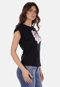 Maglietta nera a maniche corte con un design floreale nei toni del rosa e del bianco, realizzata in morbido cotone, abbinata a jeans blu.