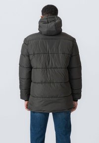 Puffjakke i mørkegrøn med høj krave, quiltet design og hætte. Har elastiske manchetter og en afslappet, let længere pasform.