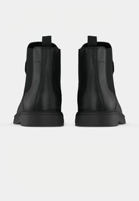 Une paire de bottines en cuir noir avec des languettes de tirage, vues de l'arrière sur un fond clair.