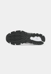 Black rubber outsole with white accents, featuring a textured tread pattern and pronounced grooves for traction and stability.