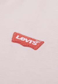 Ροζ βαμβακερό ύφασμα με κόκκινο λογότυπο Levi's, λευκή κεντητική, ορθογώνιο σχήμα και υφασμένα άκρα.