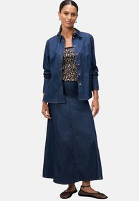 Džínová bunda s kapsami na nášivky, v kombinaci s černým květinovým topem a dlouhou džínovou sukní. Outfit doplňují černé síťované baleríny.