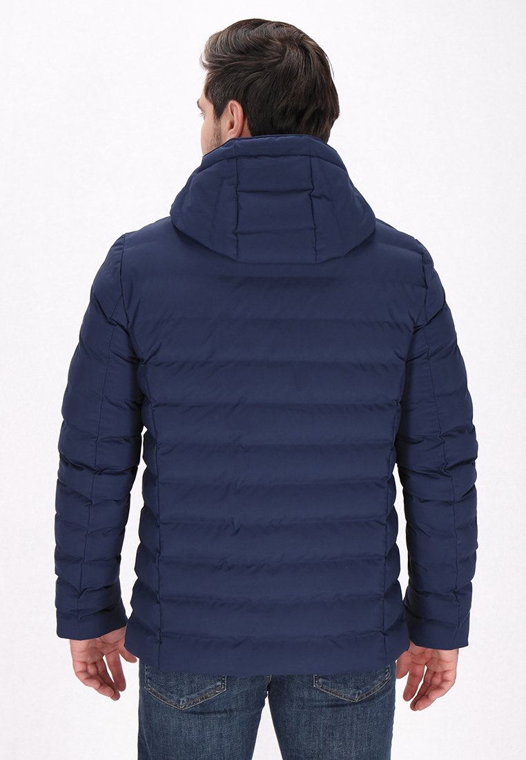 Navyblaue Steppjacke mit horizontalen Steppnähten, verstellbare Kapuze und einer glatten Textur. Über Jeans getragen.