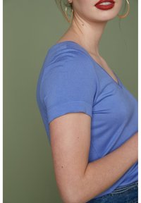 Lichtblauw V-hals t-shirt van zacht katoen met korte mouwen, gepresenteerd tegen een groene achtergrond. Heeft een getailleerd ontwerp.
