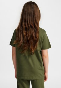 Oliwkowa bawełniana koszulka z krótkim rękawem, luźny krój i prosta konstrukcja. Tył koszulki pokazuje falujące włosy i proste detale przeszycia.