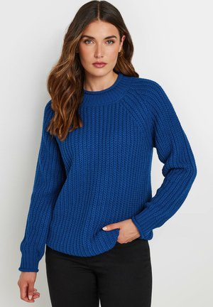 Blauwe gebreide trui met een gestructureerd, ribbelpatroon, ronde halslijn en lange mouwen; gecombineerd met zwarte broek.