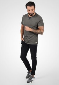 Grå T-skjorte med kort erm og V-hals, sammen med svarte jeans. Modellen har på seg grå sneakers med hvite detaljer. Synlig arm-tatovering.