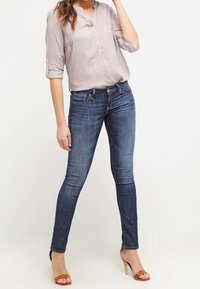 Blusa a pois grigia chiara con abbottonatura, abbinata a jeans skinny blu scuro e sandali con tacco marroni.
