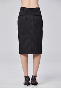 Jupe crayon noire en tissu lisse avec une taille ajustée, deux poches arrière et une coupe mi-genou. Associée à des chaussures à talons hauts noires.