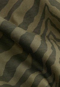 Zbliżenie na pleciony materiał w zielonym i ciemnym brązowym kamuflażu z widoczną teksturą i fałdami.