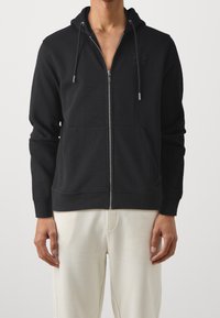 Černá mikina na zip s klokaní kapsou a kapucí se šňůrkou. Obsahuje texturované logo na hrudi a žebrované manžety. Měkký materiál.
