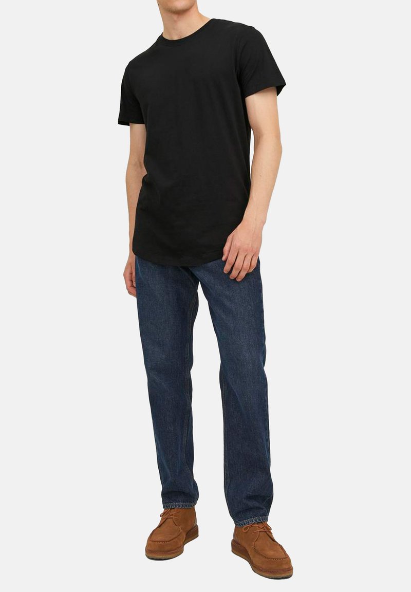 T-shirt in cotone nero a maniche corte, abbinato a jeans in denim blu. Scarpe in suede marroni con lacci e design della punta arrotondata.