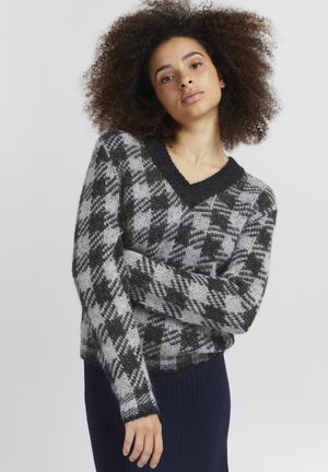 V-pään aukko, ylipitkä villapaita musta-harmaassa houndstooth-kuosissa. Pehmeä, teksturoitu neulekangas, pitkähihaisilla hihoilla ja resorireunoilla.