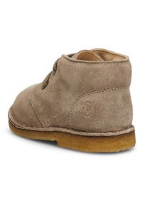 Tan mockasiner som når ankeln med rund tå, platt brun sula och minimal sömnad. Sidsnörning och logotypdetalj på hälen.