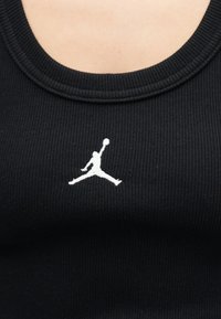 Κοντινό πλάνο μαύρου ριμπ τοπ με λευκή κεντημένη σιλουέτα καλαθοσφαιριστή που πηδά με μπάλα.