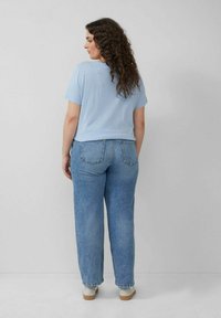 Lichtblauw t-shirt met korte mouwen gecombineerd met lichtblauwe rechte jeans, voorzien van zakken en opgerolde broekspijpen. Model zichtbaar van achteren.