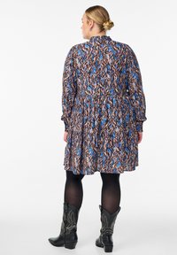 Kukkamustrinen mekko sinisen, ruskean ja kermaisen sävyisenä, tiukalla vyötäröllä ja kerroksellisella hameella. Yhdistetty mustiin cowboy-kenkihin.