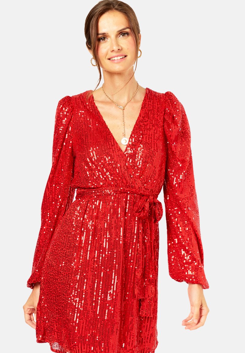 Red sequin dress with long, puffed sleeves, a deep V-neckline, and a tied waist. Drape falls to mid-thigh, featuring a shimmering texture.