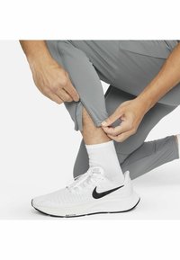 Hände ziehen den Reißverschluss am Knöchel grauer Sporthosen über weißen Socken und weißen Nike-Laufschuhen hoch.