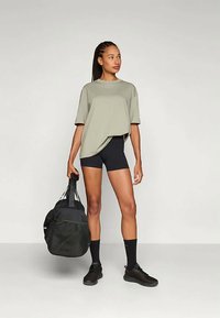 Grønn oversized t-skjorte, sorte biker-shorts, sorte joggesko og en svart duffelbag. Jevn stoff med avslappet passform. Enkel design.