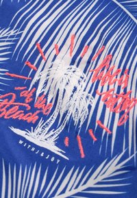 Blått tyg med broderade palmträd i vitt och korall, med text. Designen inkluderar ränder och dekorativa accenter. Hållbart, texturerat material.