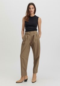 Zwart mouwloos topje, hooggewa column brown geplooide broek met taps toelopende pijpen, gecombineerd met beige haklaarsjes tot de enkel. Gladde stof en strakke lijnen.