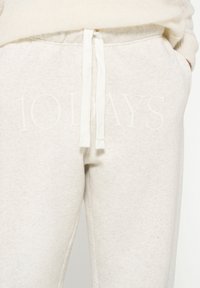 Lichtgrijze sweatpants van een zachte katoenen mix. Voorzien van een witte trekkoord en grote "10 DAGEN" tekst in een subtiele print aan de voorkant.