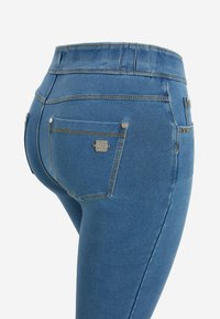 Vaqueros azules de mezclilla con cintura alta, textura suave y costuras decorativas. Incluyen dos bolsillos traseros con detalles metálicos.