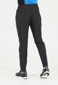 Svarta träningsbyxor med en avsmalnande design, elastisk midja, sidofickor och kontrasterande logodetaljer, i kombination med strukturerade grå sneakers.