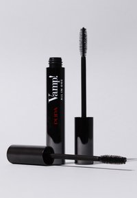 Czarna tubka tuszu do rzęs o błyszczącym wykończeniu z czerwonym napisem. Zawiera stożkową szczoteczkę z drobnymi włoskami, ustawioną pionowo obok tubki.