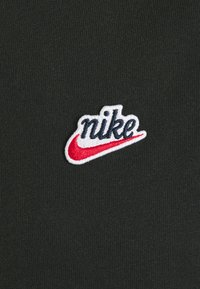 Nike logo patch on a dark green, textured fabric. The embroidered logo features white letters with red accents.