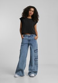 Fekete, rövidített póló felgörgő ujjakkal, széles lábú, megkopott kék farmer cargo nadrággal párosítva, amelyen folt zsebek vannak és a szegélye foszlott.