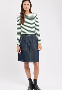 Haut rayé à manches longues en crème et vert porté avec une jupe en jean bleu foncé en forme de A dotée de deux grandes poches et de boutons dorés. Bottines noires.