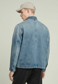 Denimjacka i ljusblått med en klassisk passform, som har krage, knappade ärmslut och synlig söm. Slät textur och strukturerad design.