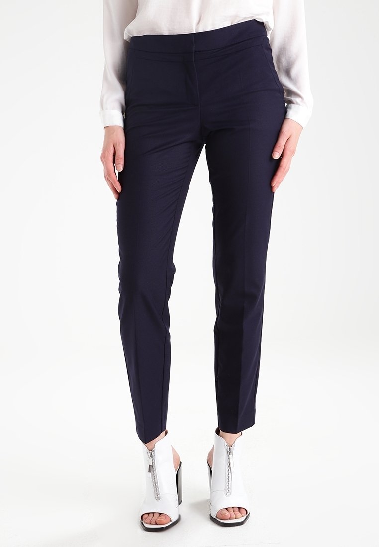 Marinblå slim-fit byxor med en mjuk textur och medelhög midja. Matchas med vita öppna högklackade skor med blixtlås.