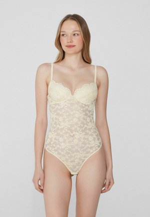 Kanten body in lichtgeel met een gekartelde rand, dunne verstelbare bandjes en een bloemenpatroon. Transparante textuur en een aansluitend ontwerp.