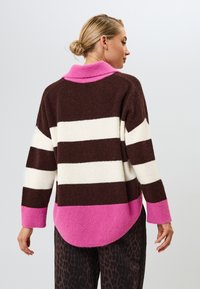 Ruskea ja valkoinen raidallinen neulepusero, jossa on vaaleanpunainen kaulus ja alahelma. Neulottu rakenne, rento malli pidemmällä selkäosalla ja hihoilla.